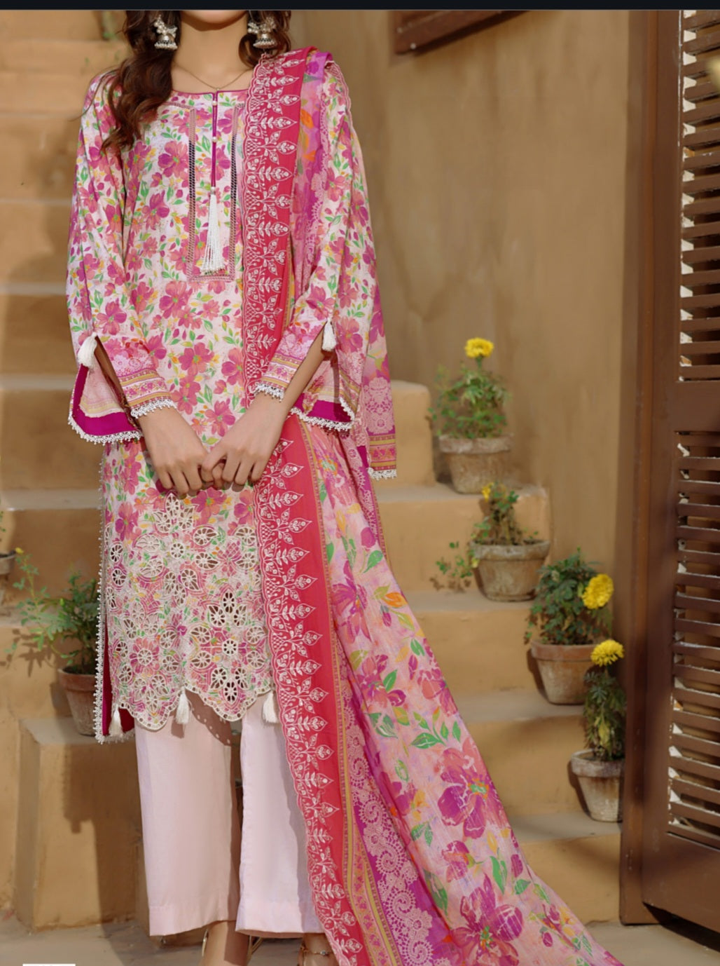 Woman wearing a pink floral embroidered outfit with a matching dupatta in an outdoor setting.